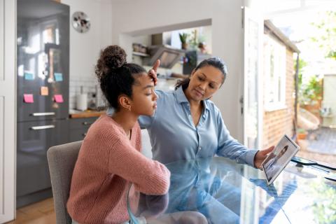 A concerned mom feels her adolescent daughter's forehand while on a pediatric telehealth call.