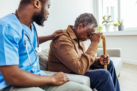 A male nursing home resident grieves and he is comforted by a nursing home employee who shares in his sorrow