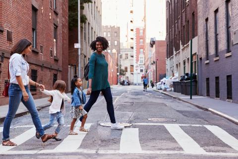 Two friends with young children cross the street in an American city.