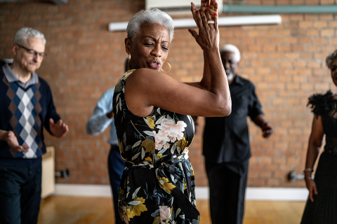 An older woman dancing in the center of a group of other older people.