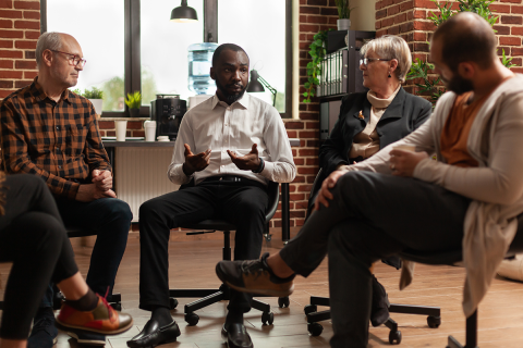 A man talking while in the center of a group of people.