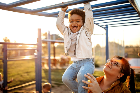 Child playing on monkey bars while a woman is carrying him.