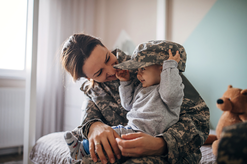 Woman in a military uniform holding a child with a military hat on.